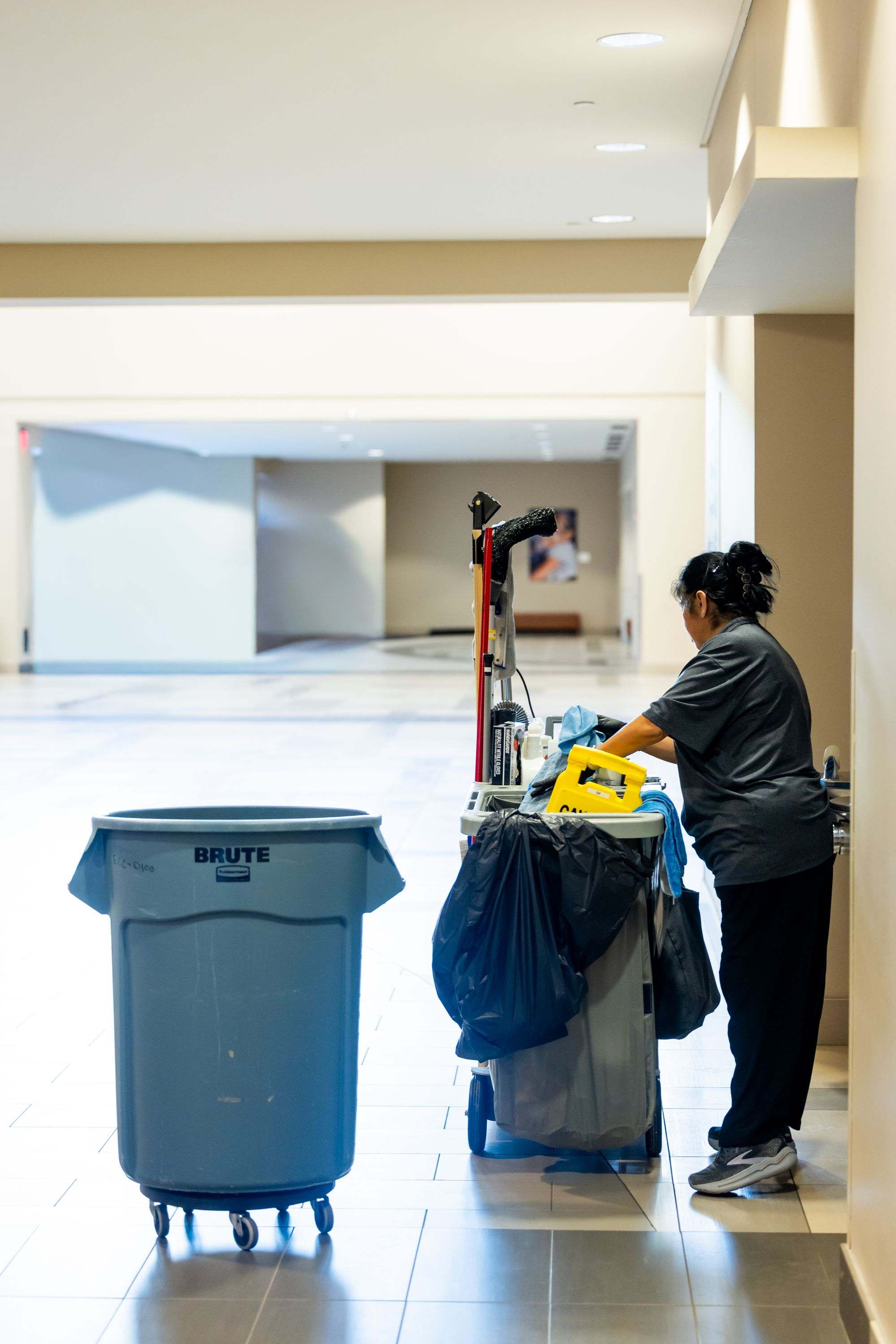 A cleaner working from a janitorial cart in a bright, spacious commercial hallway
