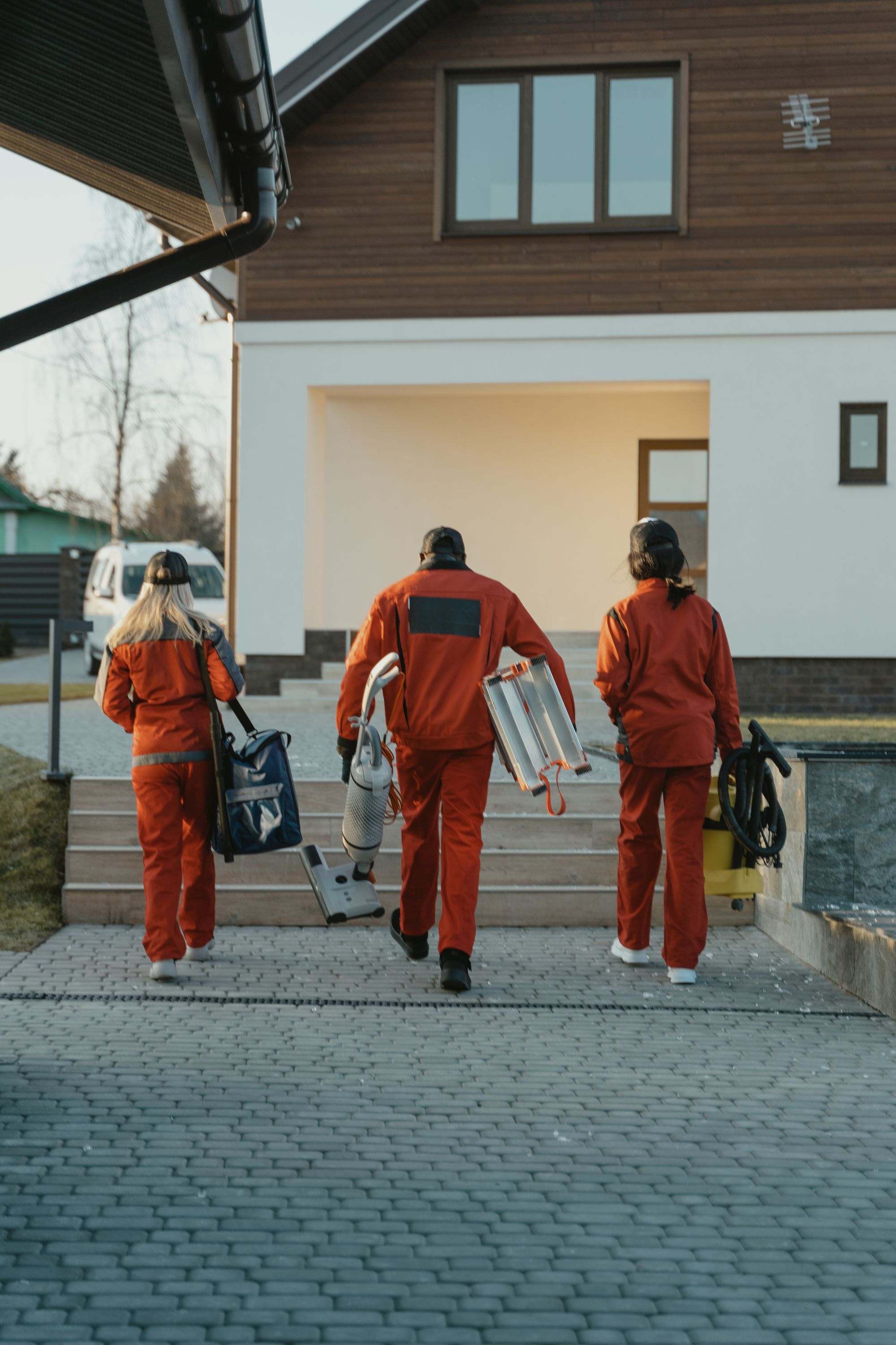 A cleaning crew in red uniforms carrying equipment up to a house, arriving for a call-out