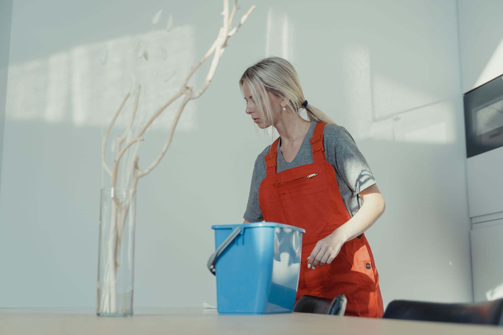 A cleaner in a red uniform working with a bucket of supplies in a bright modern room