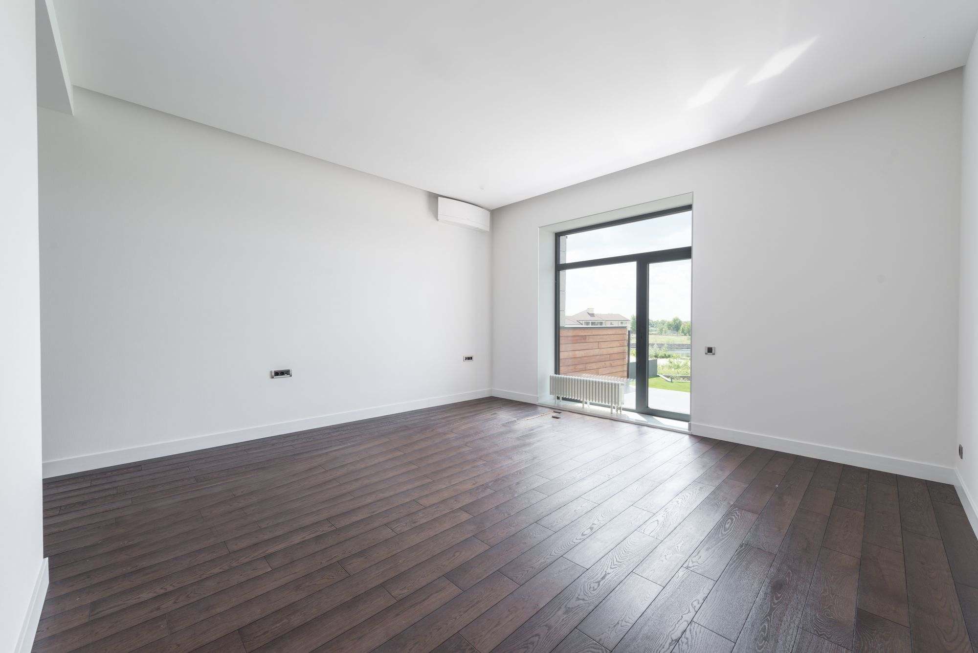 A bright, empty apartment room with a polished wooden floor, cleaned and ready to move into